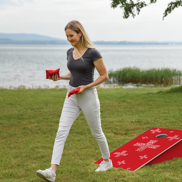 Frau mit Wurfsäckchen neben rotem Cornhole-Brett am See